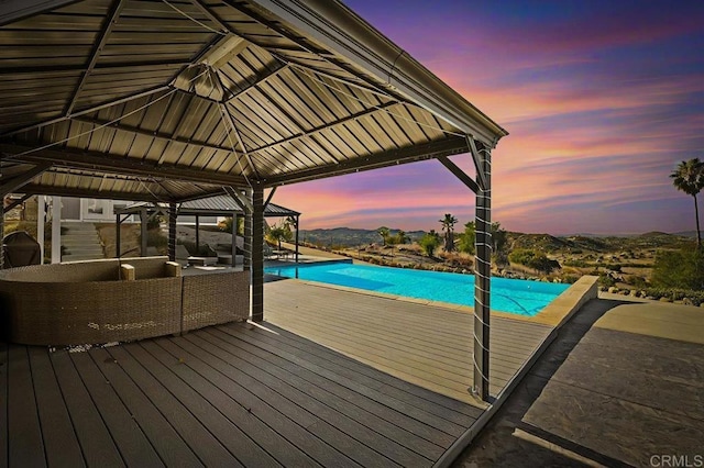 pool at dusk with a mountain view, a gazebo, and an outdoor hangout area