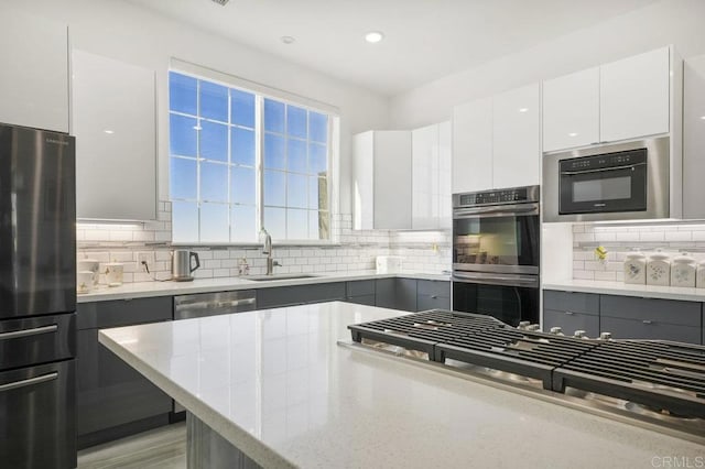 kitchen featuring decorative backsplash, appliances with stainless steel finishes, sink, and white cabinetry