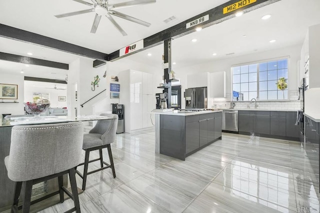 kitchen featuring a spacious island, appliances with stainless steel finishes, white cabinetry, ceiling fan, and beam ceiling