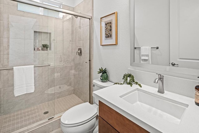 bathroom with a shower with shower door, toilet, and vanity