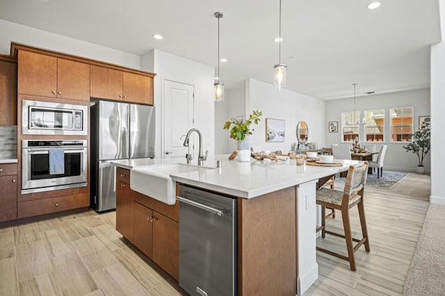 kitchen featuring pendant lighting, appliances with stainless steel finishes, an island with sink, sink, and a kitchen breakfast bar