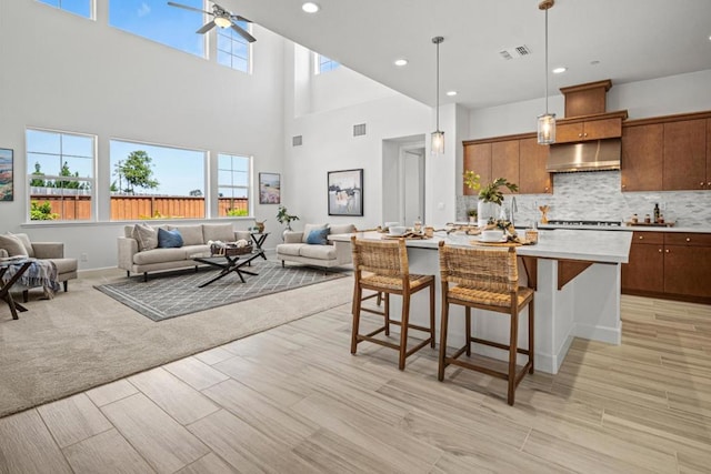 kitchen featuring pendant lighting, wall chimney exhaust hood, a kitchen bar, backsplash, and a kitchen island with sink