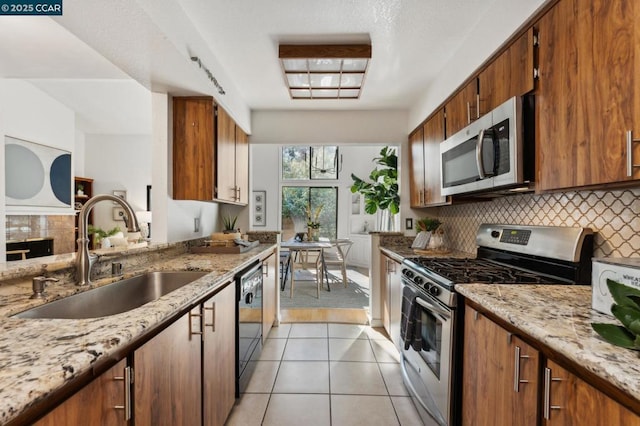 kitchen featuring light tile patterned floors, appliances with stainless steel finishes, backsplash, light stone counters, and sink