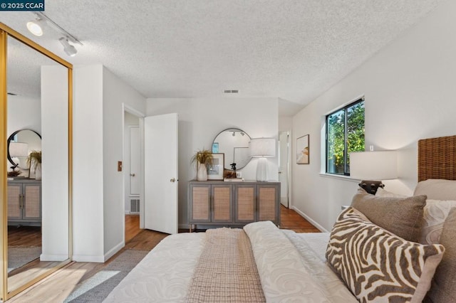 bedroom with a textured ceiling, track lighting, and light hardwood / wood-style floors