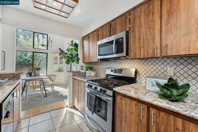 kitchen with light stone countertops, backsplash, light tile patterned floors, and stainless steel appliances