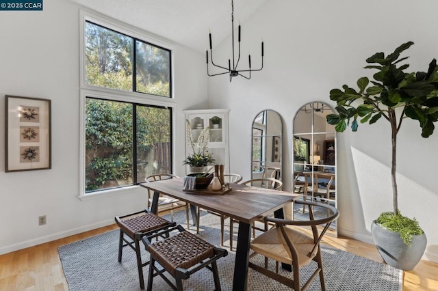 dining room featuring light wood-type flooring, a chandelier, a towering ceiling, and plenty of natural light