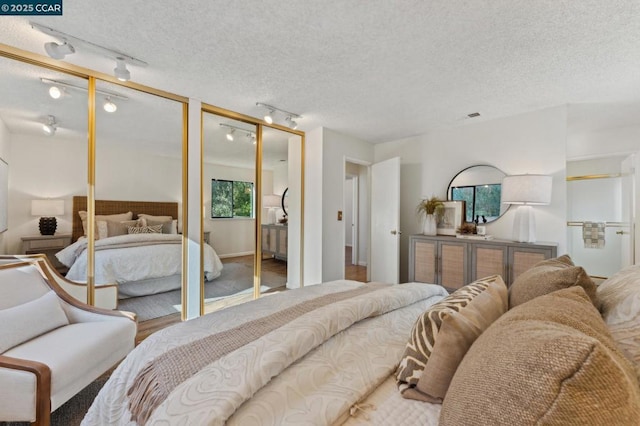 bedroom featuring rail lighting, a textured ceiling, and multiple closets