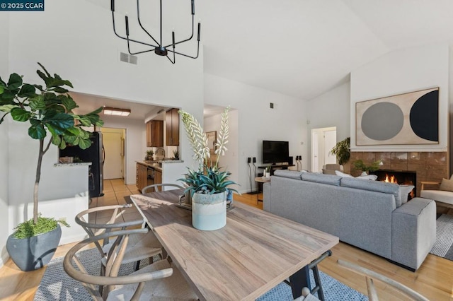 dining area with a tiled fireplace, lofted ceiling, light hardwood / wood-style flooring, and a notable chandelier