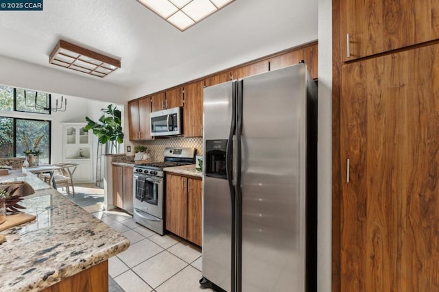 kitchen with light stone countertops, light tile patterned floors, backsplash, and appliances with stainless steel finishes