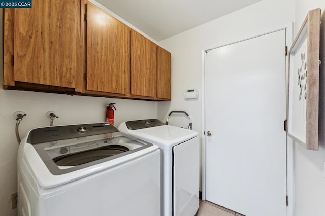 clothes washing area featuring light tile patterned floors, washing machine and dryer, and cabinets