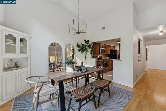 dining area with high vaulted ceiling, a chandelier, and light wood-type flooring