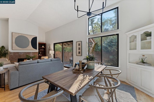 dining area featuring a chandelier, light hardwood / wood-style floors, a tiled fireplace, and high vaulted ceiling