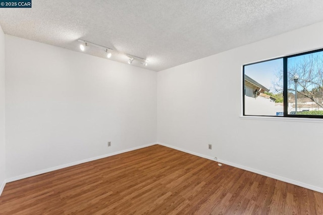 spare room featuring rail lighting, a textured ceiling, and hardwood / wood-style flooring