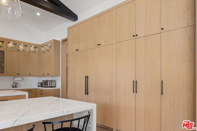 kitchen featuring decorative backsplash, light brown cabinetry, vaulted ceiling with beams, light stone counters, and a breakfast bar