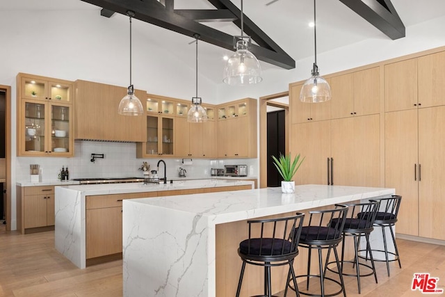 kitchen featuring tasteful backsplash, a spacious island, decorative light fixtures, light stone counters, and beamed ceiling