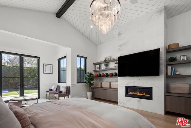 bedroom with lofted ceiling with beams, a high end fireplace, a chandelier, and light hardwood / wood-style flooring