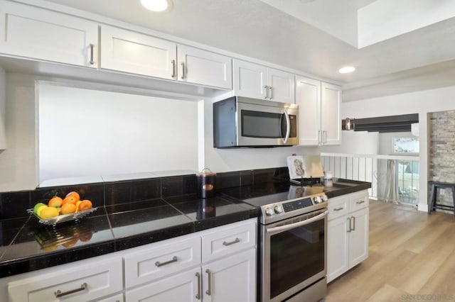 kitchen with light wood-type flooring, appliances with stainless steel finishes, and white cabinetry