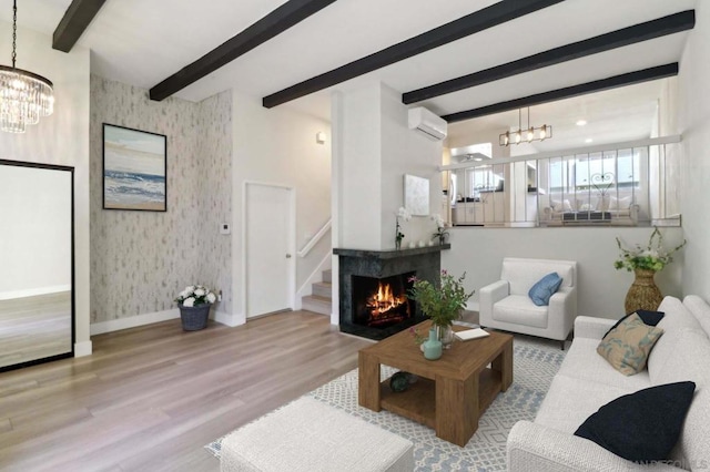 living room featuring a wall mounted AC, light hardwood / wood-style floors, a notable chandelier, a multi sided fireplace, and beamed ceiling