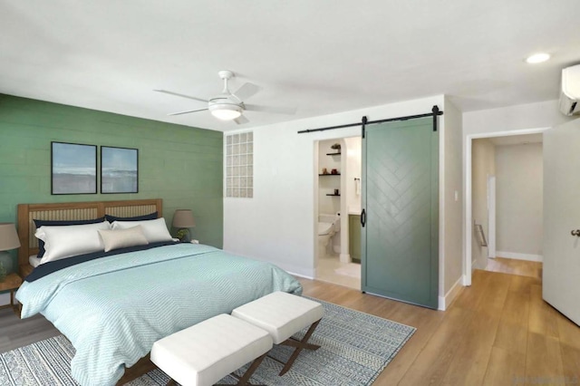 bedroom featuring ceiling fan, a barn door, an AC wall unit, light hardwood / wood-style floors, and ensuite bath