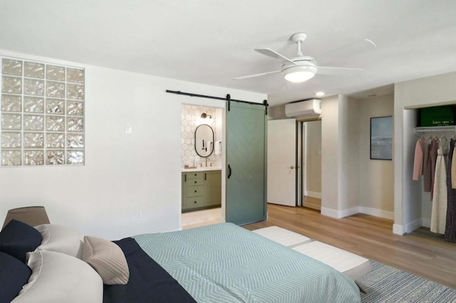 bedroom featuring ensuite bathroom, a barn door, a wall unit AC, ceiling fan, and a closet