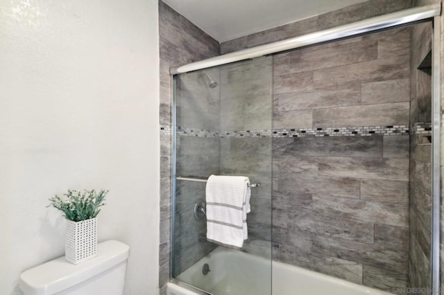 bathroom featuring toilet and shower / bath combination with glass door