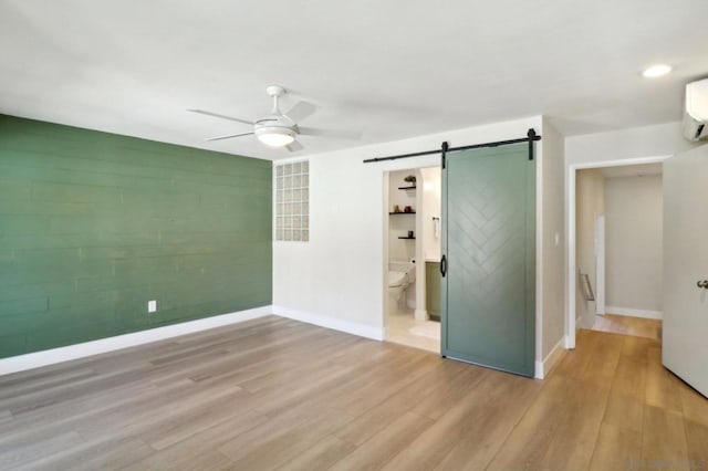 empty room with ceiling fan, light hardwood / wood-style flooring, a barn door, and a wall mounted air conditioner