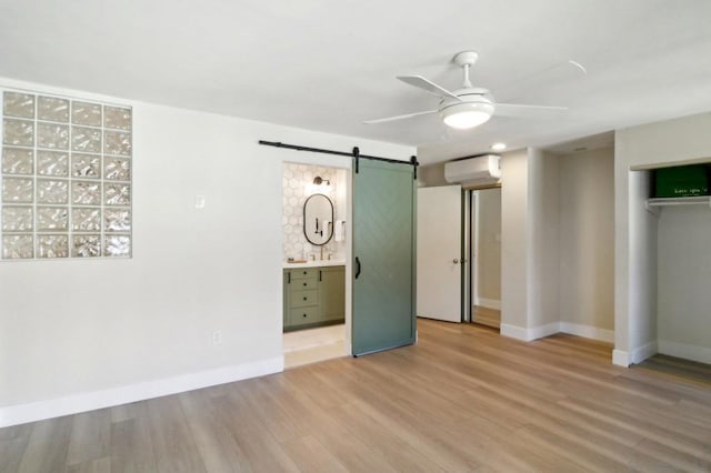 unfurnished bedroom with a barn door, ceiling fan, ensuite bath, a wall mounted air conditioner, and a closet