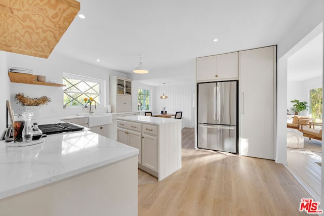 kitchen featuring white cabinetry, stainless steel fridge, light wood-type flooring, light stone counters, and sink