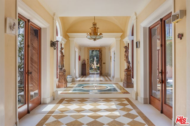 hallway featuring french doors, a notable chandelier, and ornate columns