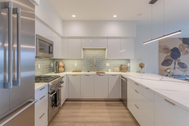 kitchen featuring white cabinets, hanging light fixtures, kitchen peninsula, light stone counters, and high quality appliances