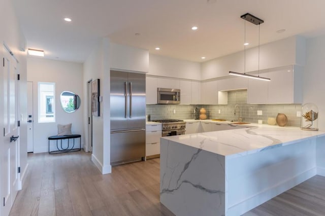 kitchen featuring decorative light fixtures, white cabinetry, high end appliances, kitchen peninsula, and light wood-type flooring