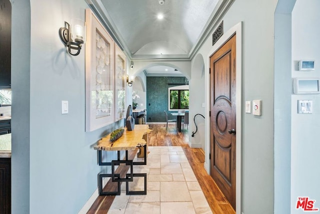 corridor with lofted ceiling, crown molding, and light hardwood / wood-style flooring