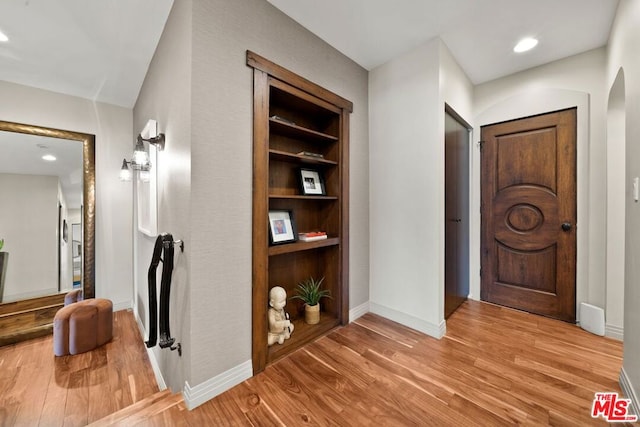 corridor with light hardwood / wood-style floors and built in shelves