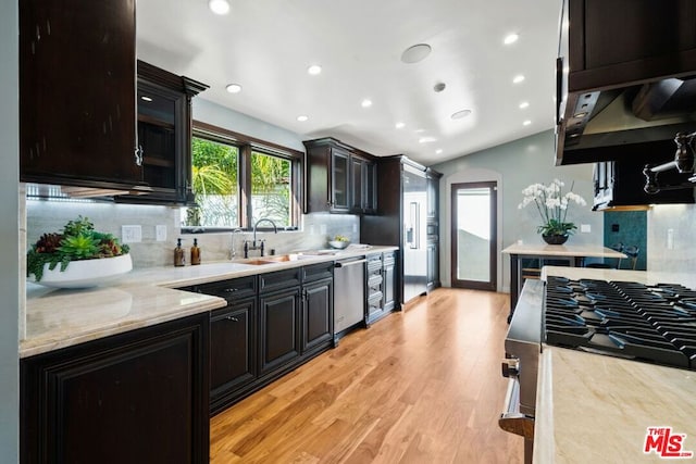 kitchen with appliances with stainless steel finishes, decorative backsplash, sink, light stone counters, and light hardwood / wood-style flooring