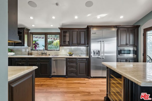 kitchen with decorative backsplash, sink, built in appliances, light wood-type flooring, and beverage cooler