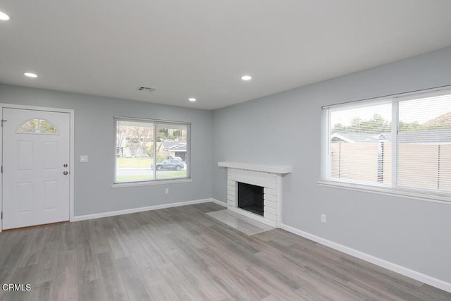 unfurnished living room featuring a brick fireplace and light hardwood / wood-style flooring