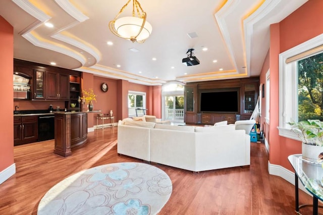 living room with wet bar, a tray ceiling, light hardwood / wood-style flooring, and crown molding