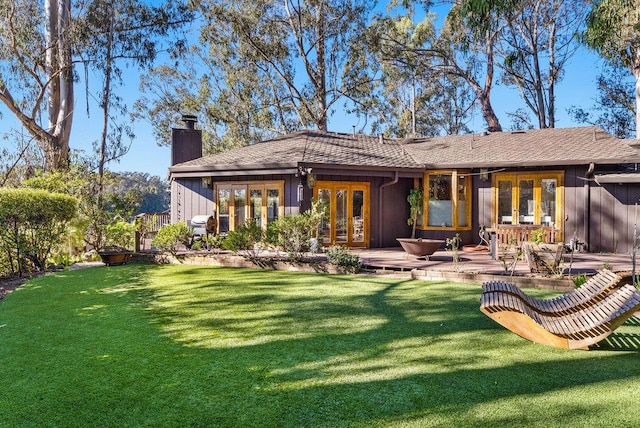 back of property with french doors, a wooden deck, and a lawn