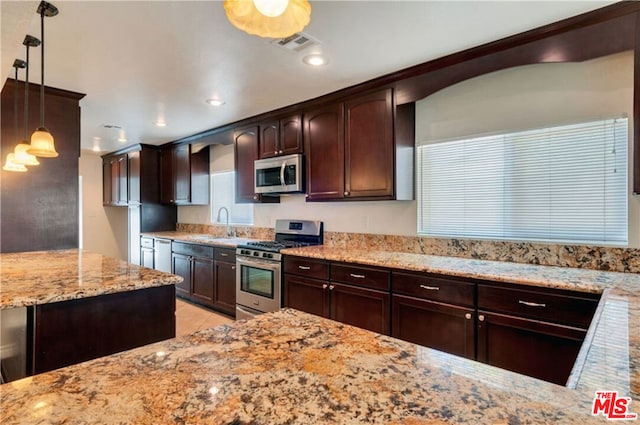 kitchen with pendant lighting, appliances with stainless steel finishes, dark brown cabinetry, sink, and light stone counters