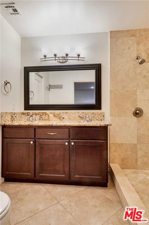 bathroom with vanity, toilet, tiled shower, and tile patterned floors