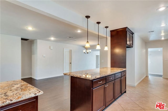 kitchen featuring hanging light fixtures, a center island, dark brown cabinets, and light stone countertops