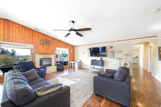 living room featuring dark wood-type flooring, wood walls, and a healthy amount of sunlight