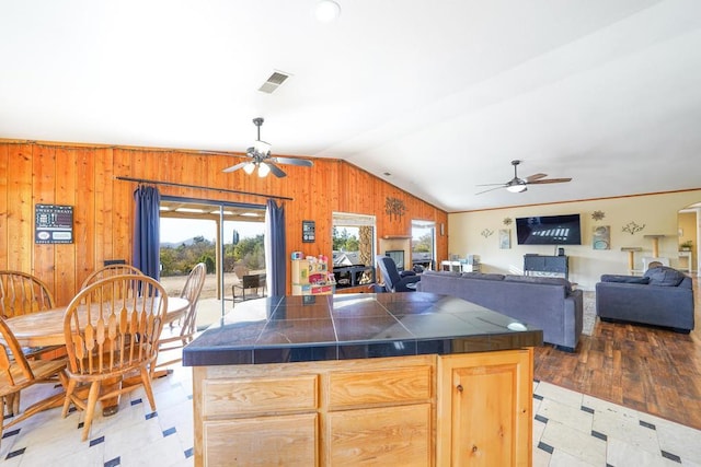 kitchen featuring vaulted ceiling, tile countertops, light brown cabinets, and wooden walls