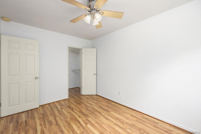 unfurnished bedroom with a closet, ceiling fan, a spacious closet, and light wood-type flooring