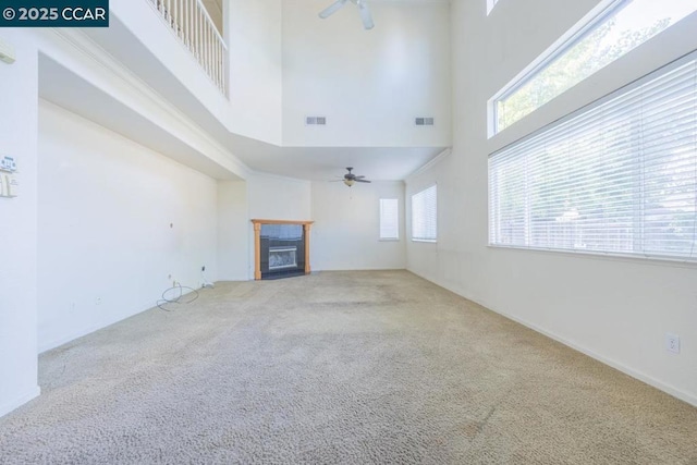 unfurnished living room with ceiling fan, a high ceiling, and carpet flooring