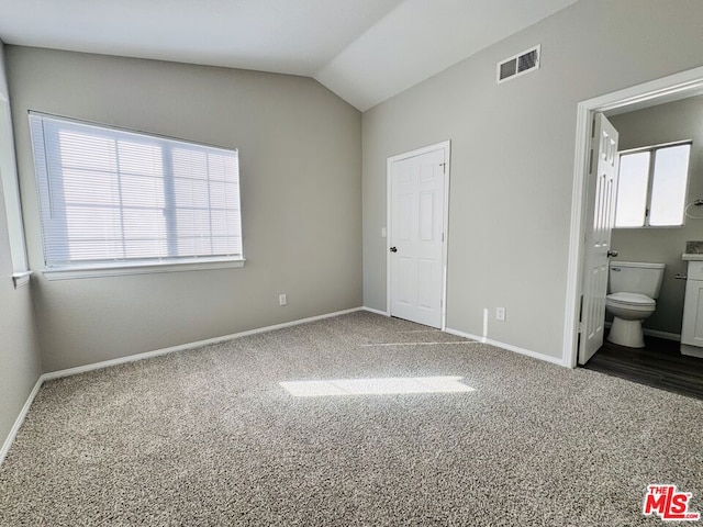 unfurnished bedroom featuring vaulted ceiling, connected bathroom, and dark colored carpet