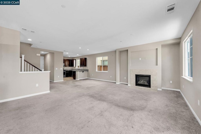 unfurnished living room featuring light carpet and a tiled fireplace