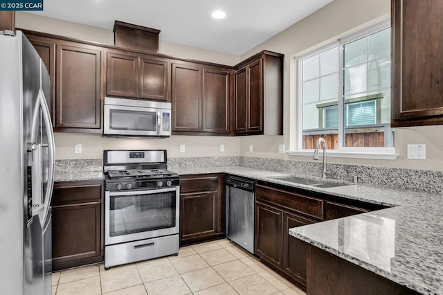 kitchen featuring sink, dark brown cabinetry, light stone countertops, appliances with stainless steel finishes, and light tile patterned floors