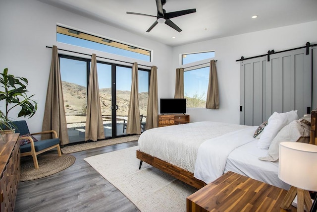 bedroom featuring ceiling fan, access to exterior, a barn door, and wood-type flooring