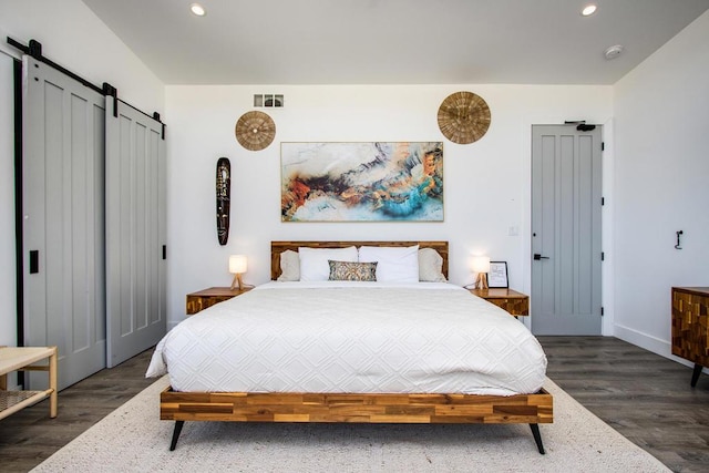 bedroom with a barn door and dark wood-type flooring